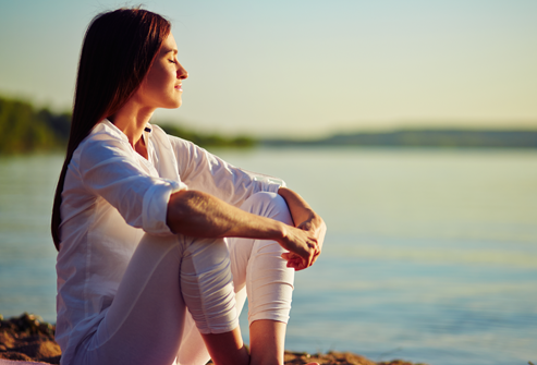Woman sitting peacefully near the water representing self-reflection, emotional healing, and personal growth.