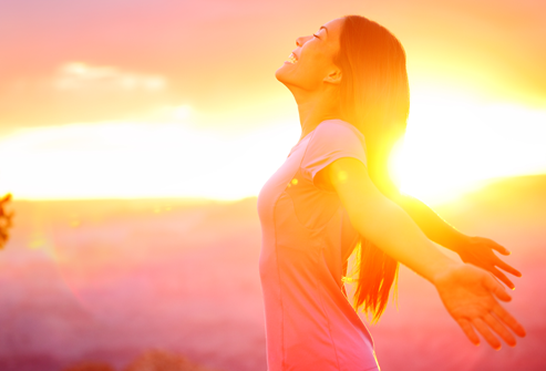 Woman outdoors with arms open at sunset representing mindfulness, healing, and emotional wellness.